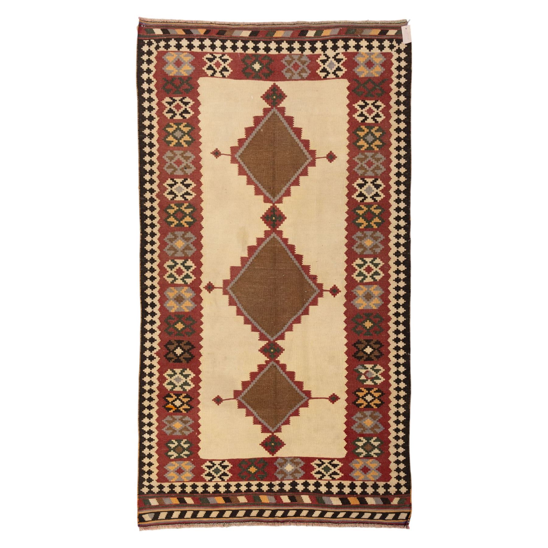 South West Persian Qashqai kilim, woven in flatweave in earthy tones, camel brown, ivory, olive, green, black, and madder red with three bold lozenge-shaped medallions, geometric borders incorporating stepped, hooked, and rosette motifs 