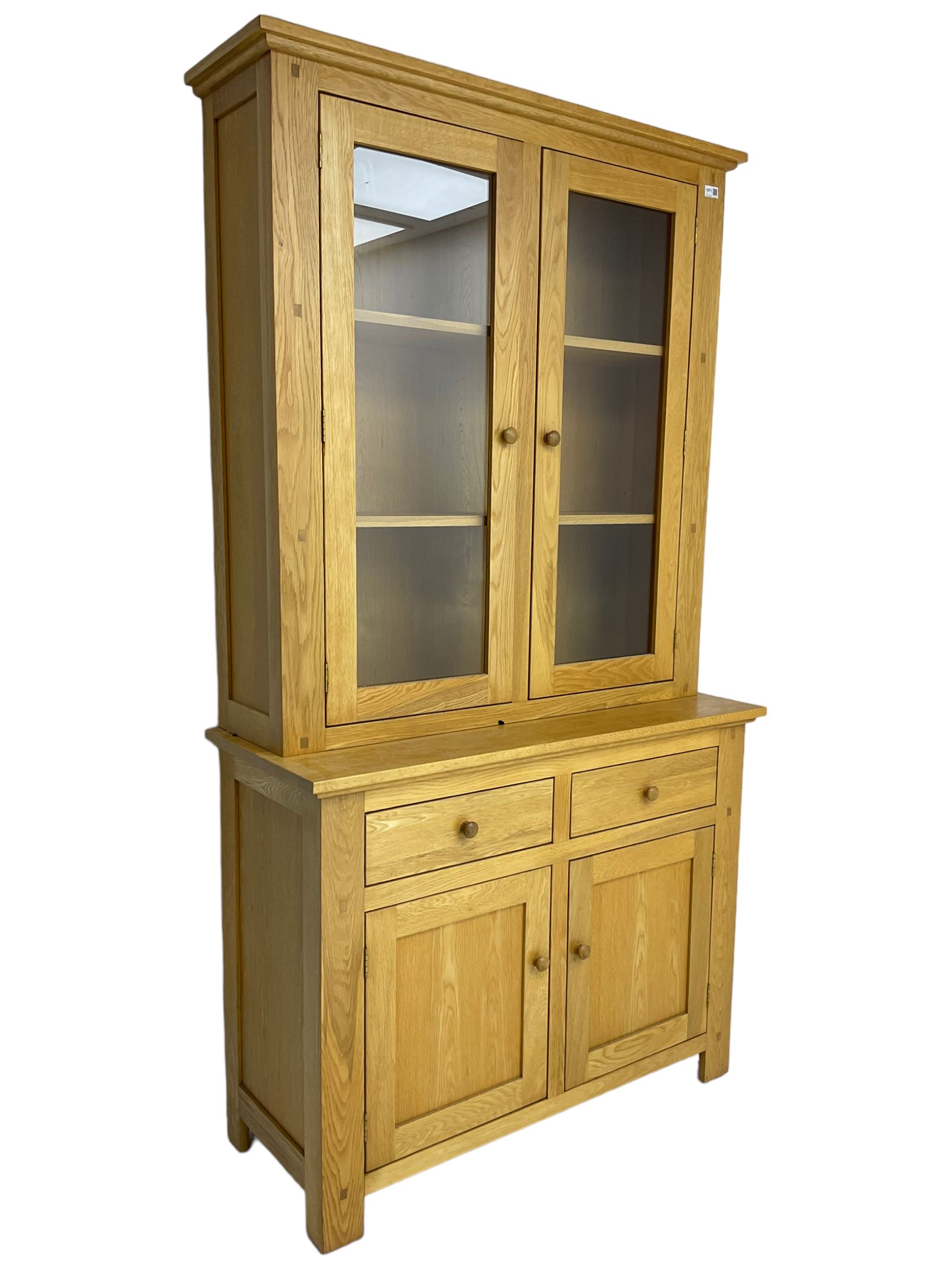 Contemporary light oak bookcase display cabinet, fitted with  two glazed doors enclosing two shelves, above two drawers and cupboards