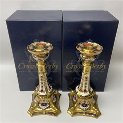 Pair of modern Royal Crown Derby Old Imari 1128 pattern candlesticks, each with shaped drip tray affixed to squat socket, upon spreading stem and canted square base with gilt dolphin edges, with printed marks beneath including Roman numeral year cypher for 2003, H26.5cm, with original boxes