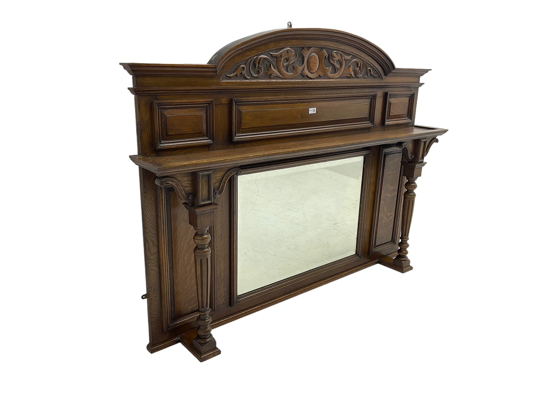 Oak overmantle mirror, arched pediment carved with shield and flanking fish with trailing scrollwork, panelled frieze over extending canopy raised by turned and fluted column pilasters, bevelled mirror plate 