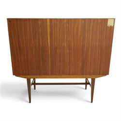 Alfred Cox - mid-20th century teak cabinet, rectangular top over two bifold doors with inset handles, opening to reveal three central graduating drawers surrounded by assorted shelves, raised on tapering supports united by H-stretcher, stamped to inside of drawer