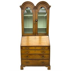 George III oak bookcase on bureau, the double arched top enclosed by two shaped glazed doors, fall-front concealing fitted interior, over four graduating cock-beaded drawers, on bracket feet