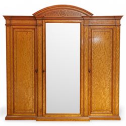 Victorian neoclassical style satinwood triple-section wardrobe, the central mirror section and arched pediment with carved monogram flanked by two panelled crossbanded doors, revealing two drawers and grooves for shelves, the hanging cupboards each with a single drawer, the whole supported on a plinth base
