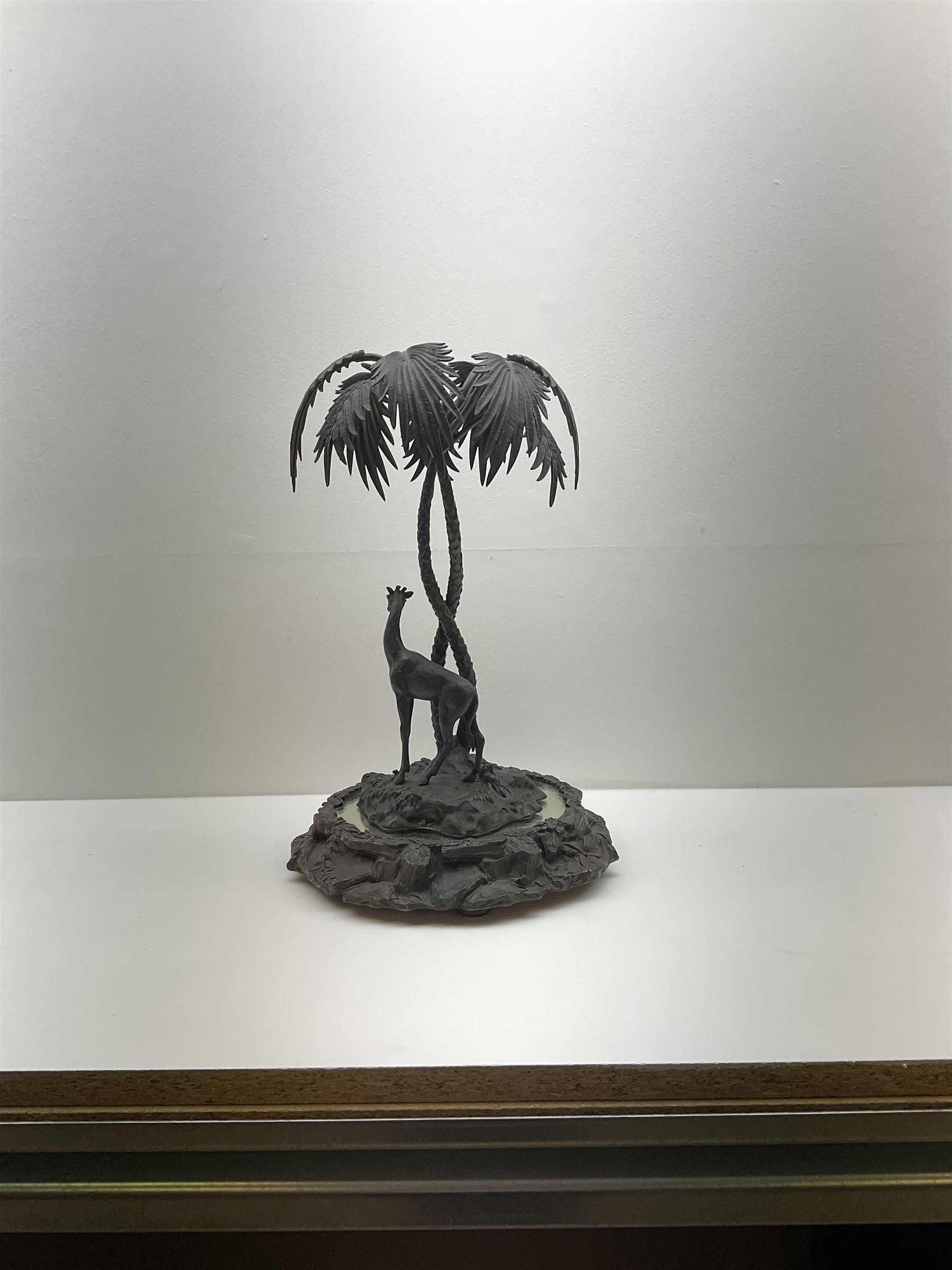 Sculpture of a giraffe under a palm tree upon a mirrored base, H48cm