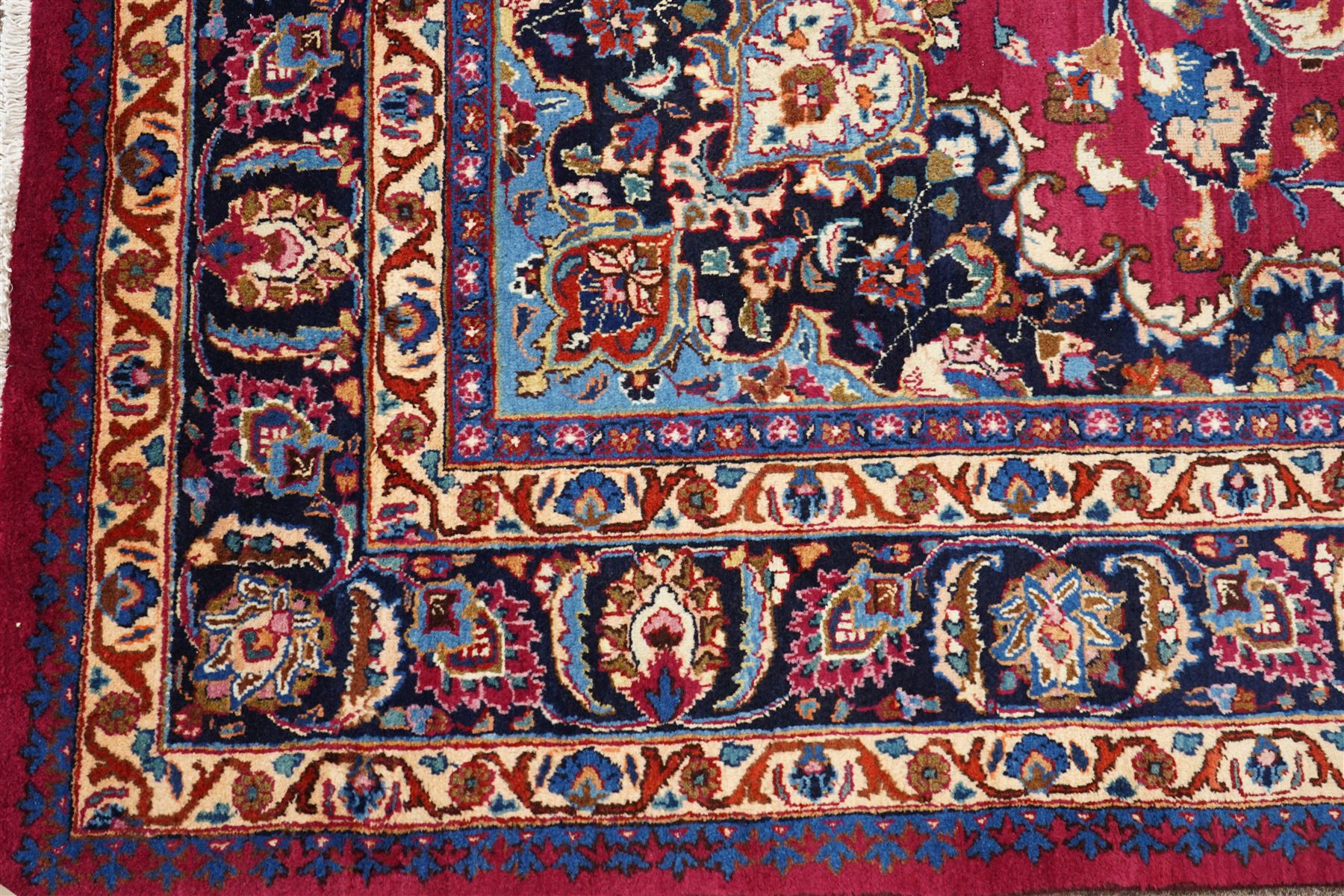 Central Persian Kashan hand-knotted carpet, rose red field, with central shaped lobed medallion issuing an all-over scrolling design of palmettes, floral sprays and arabesques, within conforming spandrels, enclosed by a broad indigo herati type palmette border framed by multiple guard stripes, in a palette of deep red, midnight blue and ivory tones, with cotton fringe ends, and Kashan signature 