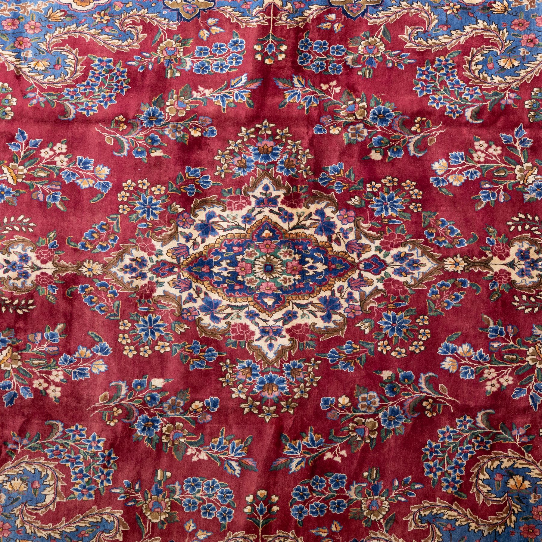 Large Central Persian Kirman hand-knotted carpet, raspberry red field, with central shaped medallion surrounded by an intricate arrangement of scrolling vines and floral sprays, within conforming spandrels and a pale blue border decorated with floral motifs, enclosed by guard stripes, with cotton fringe ends 