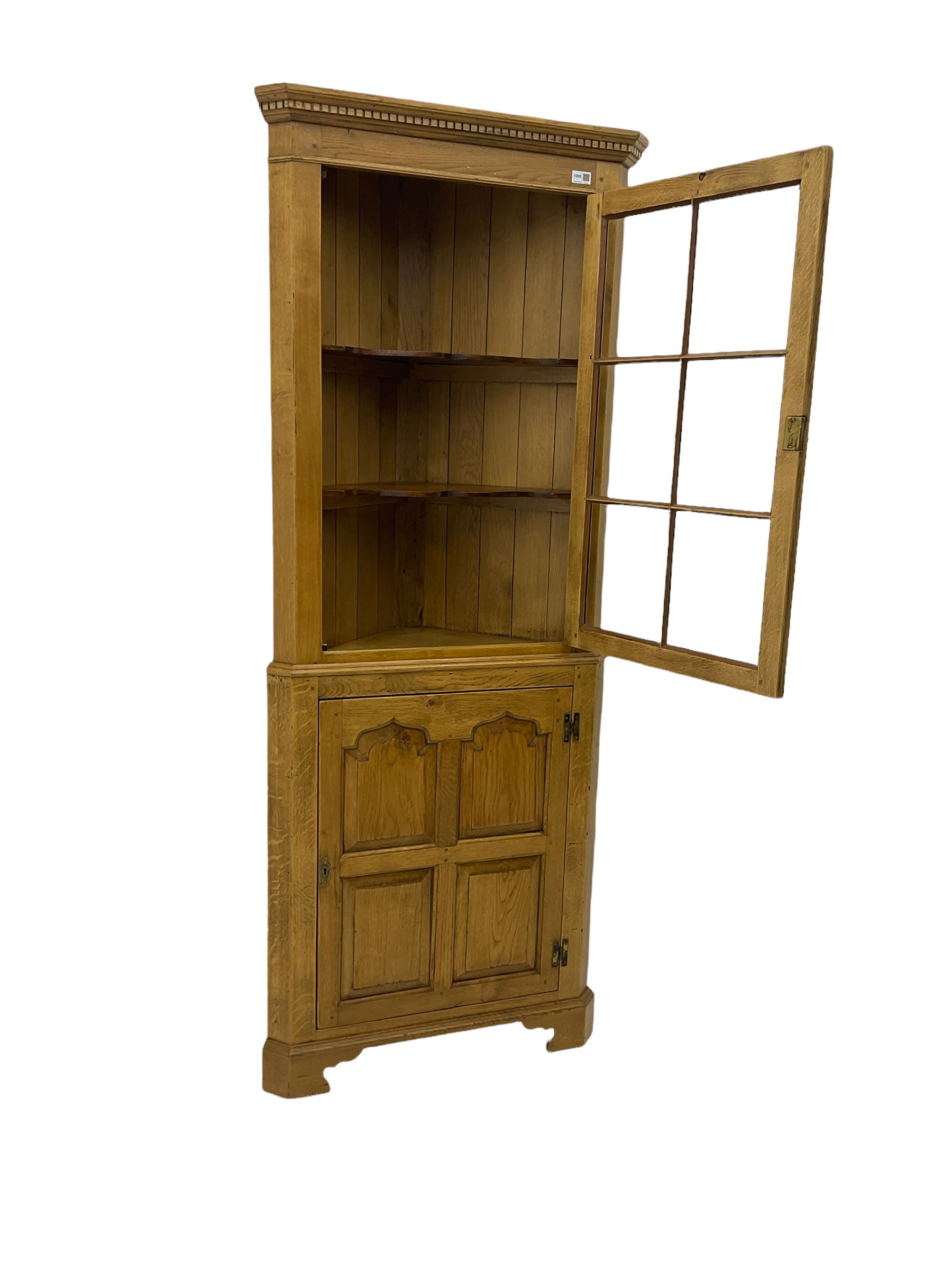Traditional light oak corner cabinet, projecting cornice, dentil frieze, single glazed door above single fielded door