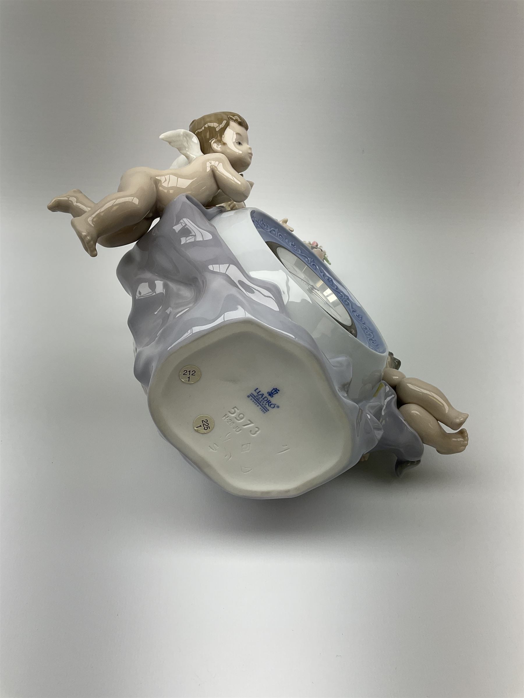 A Lladro mantel clock modelled as a globe with inset clock, surmounted by four putti and floral garlands, with blue printed mark and impressed 5973 beneath, H29cm.