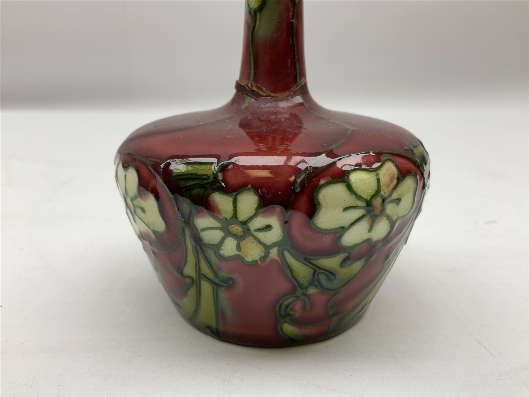 Three Minton Secessionist vases, with tube-lined stylised flower decoration, two upon a red ground and third upon a purple ground, all with printed mark to base 'Minton Ltd, No. 33', H13cm