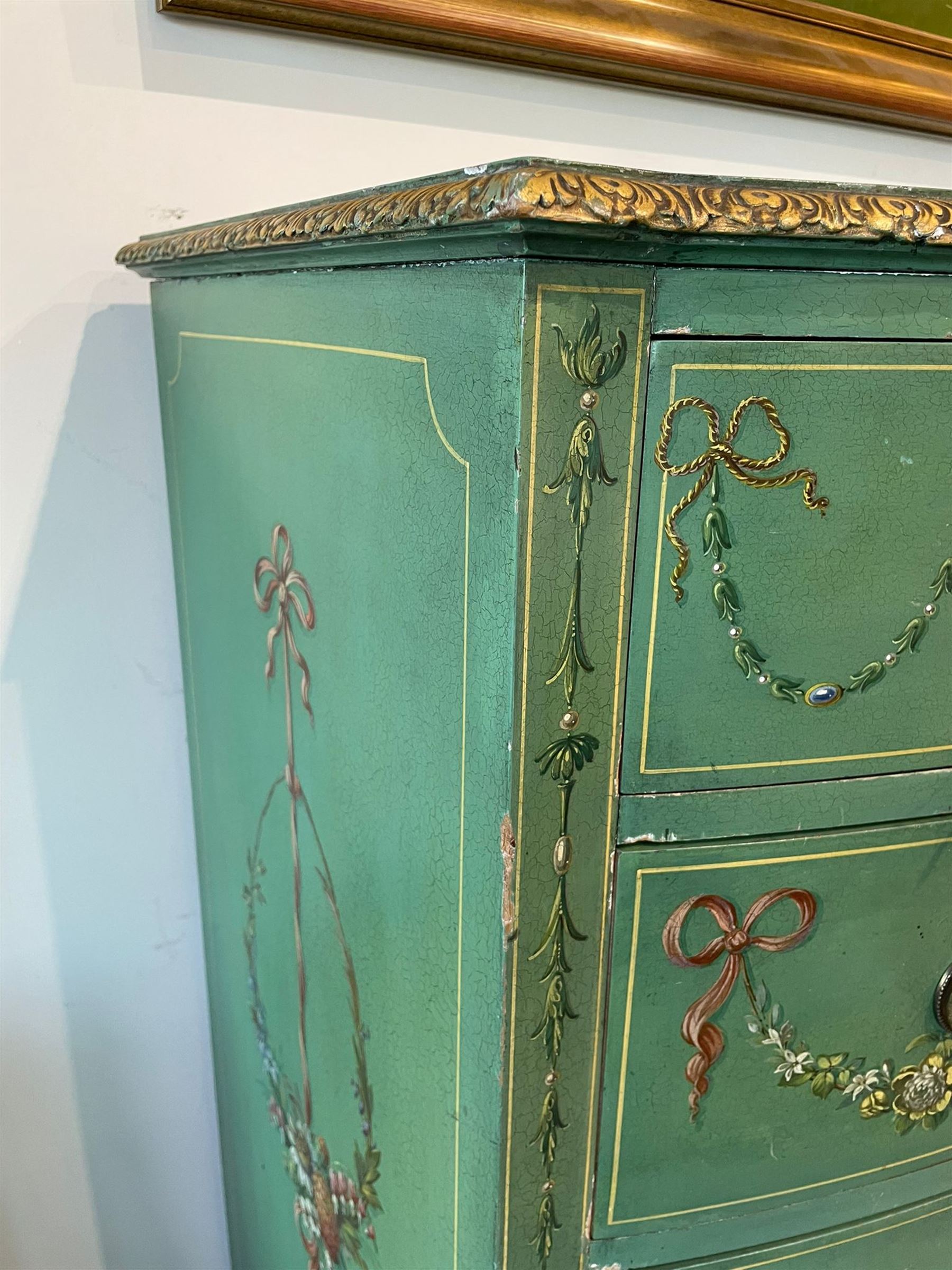 Edwardian Adam Revival green-painted and parcel gilt bowfront chest, moulded and foliate carved top painted with trailing floral band, fitted with four drawers decorated with trailing floral festoons, ribbon ties and urns, oval handle plates with engraved decoration and bead cast handles, on turned supports decorated with acanthus leaves and draped festoons 
