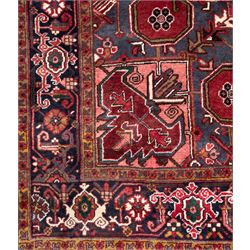 Northwestern Persian Heriz hand-knotted carpet, madder red field with a bold stepped medallion in indigo, ivory, and ivory, surrounded by angular floral motifs and stylized leaves, and the spandrels set within a dark border of rosettes and angular vine motifs, 335cmx252cm