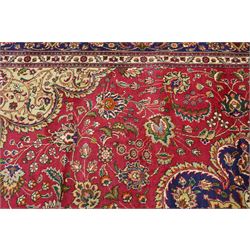 North East Persian Meshad hand-knotted carpet, crimson field with central lobed medallion in tones of indigo, ivory and soft blue, with an all-over arrangement of scrolling vinery, palmettes, and floral  sprays, conforming spandrels, main border of stylized floral vinery framed by multiple guard borders, with cotton fringe ends