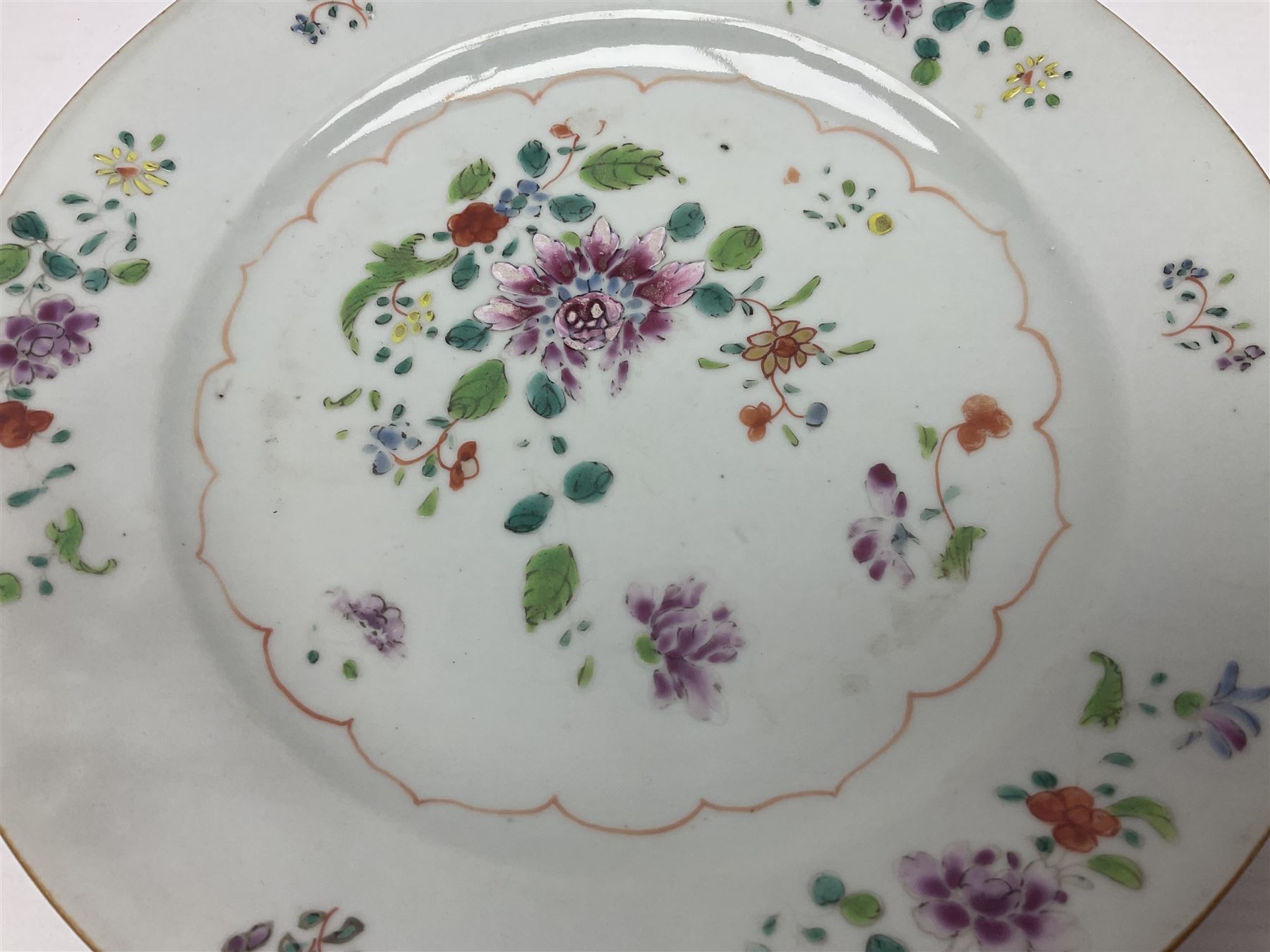 Three 18th century Chinese Famille Rose plates, the first example enamelled with blossoming peonies, rockwork and fence, the other two examples of similar design, decorated with blossoming peonies and sprigs within shaped inner borders, each approximately D23cm