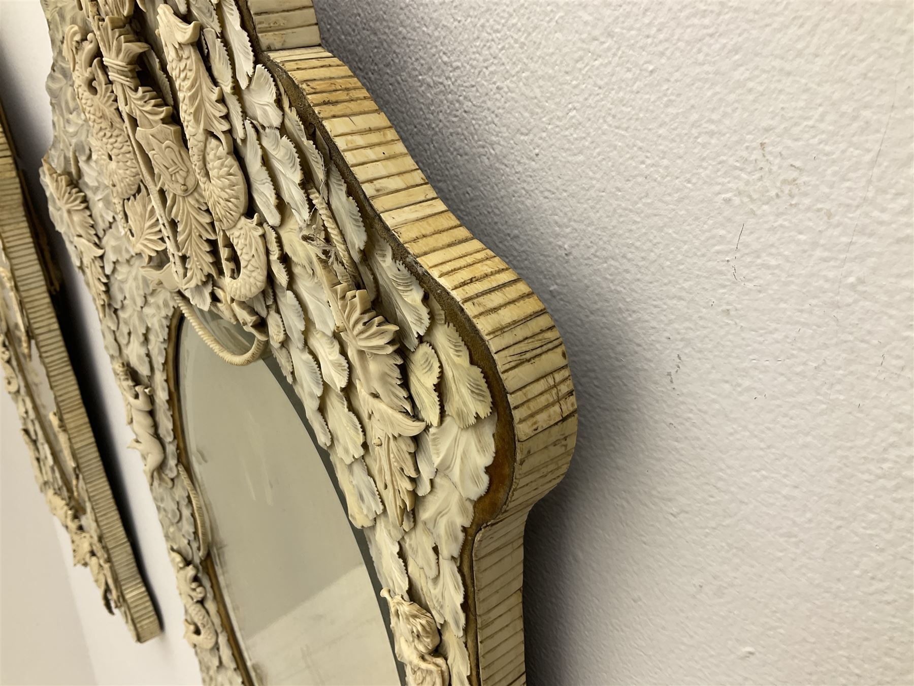 Pair 19th century French Dieppe bone and ivory wall mirrors, the oval bevelled mirror plates within rectangular frames with shaped tops, profusely decorated with ivory leaves, further detailed with carved bone armorial type crest inscribed 'SGOTORVM', putti, fish and mask heads, H81cm W48cm