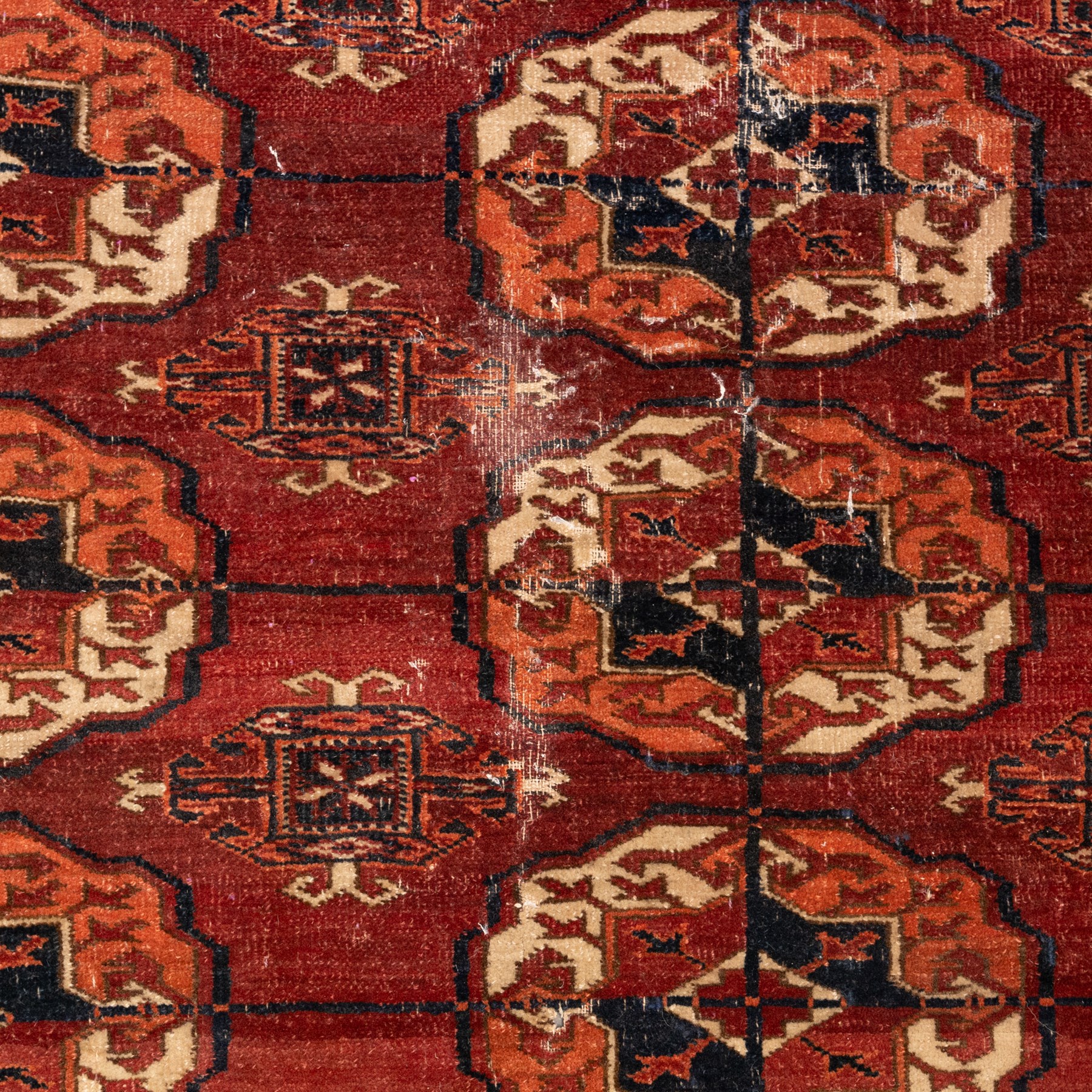 Persian Bokhara crimson ground rug, the field decorated with five rows of repeating Gul motifs with interspersed geometric design, enclosed by a guard band of further geometric-style Gul designs comprised of hook motifs