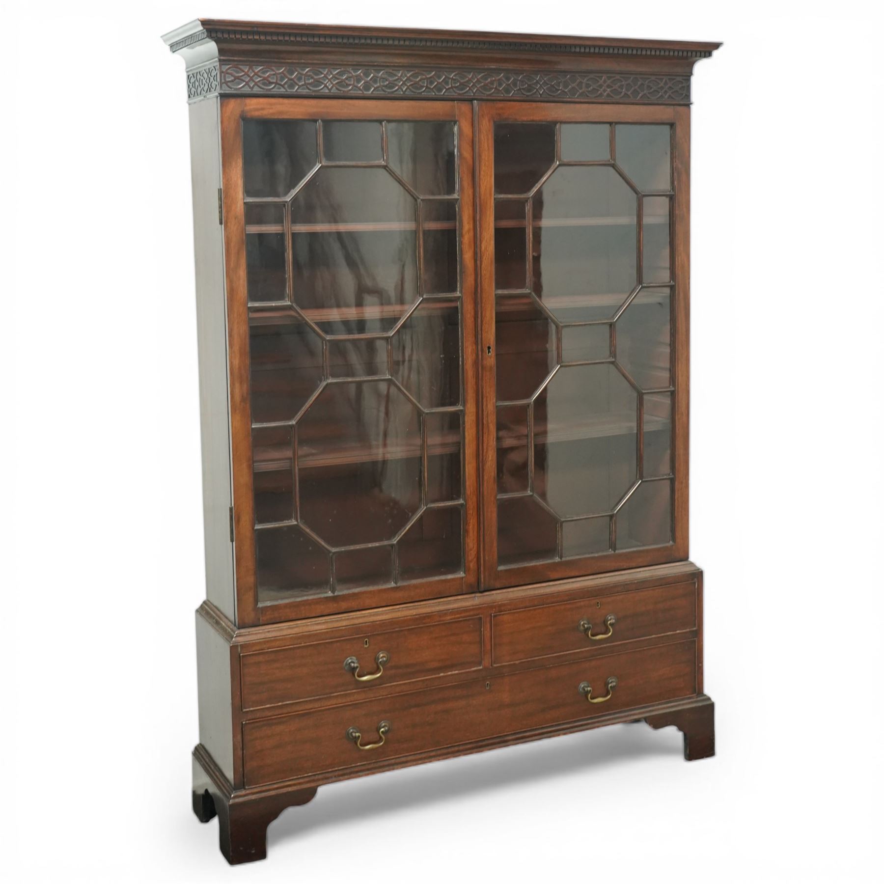 Early 20th century mahogany glazed bookcase, the moulded cornice above a carved frieze with interlaced ornament, enclosed by a pair of astragal glazed doors with geometric glazing bars, the base fitted with two short over two long drawers with brass swan neck handles, raised on bracket feet