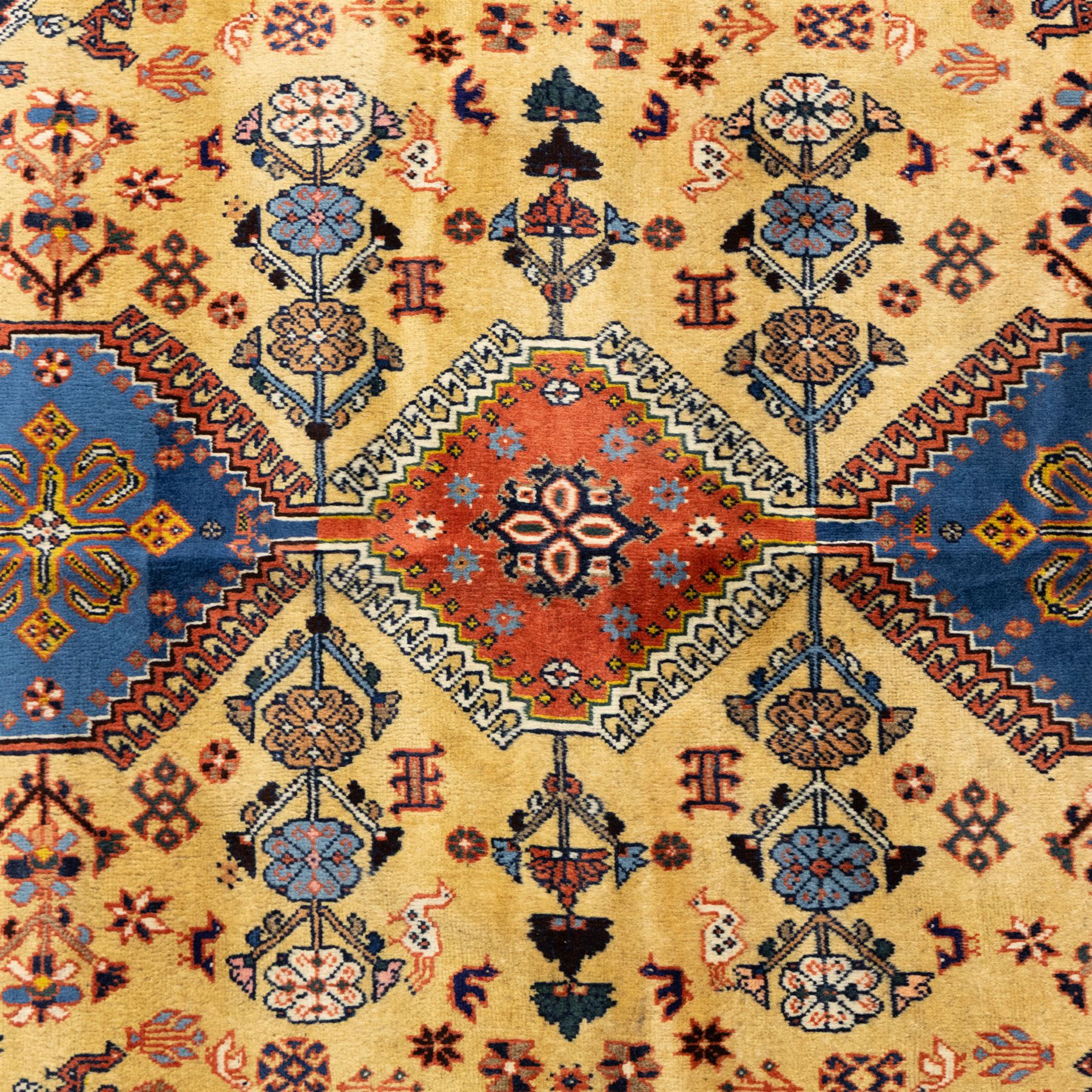 South Persian Yallameh hand-knotted rug, ivory ground, with a central stepped pole medallion design in blue and terracotta tones, surrounded by geometric tribal motifs incorporating stylised flowerheads, birds, hooked devices and angular vine work, enclosed by dark navy spandrels and a terracotta border with repeating geometric motifs, flanked by narrow patterned guard stripes, with cotton fringes
