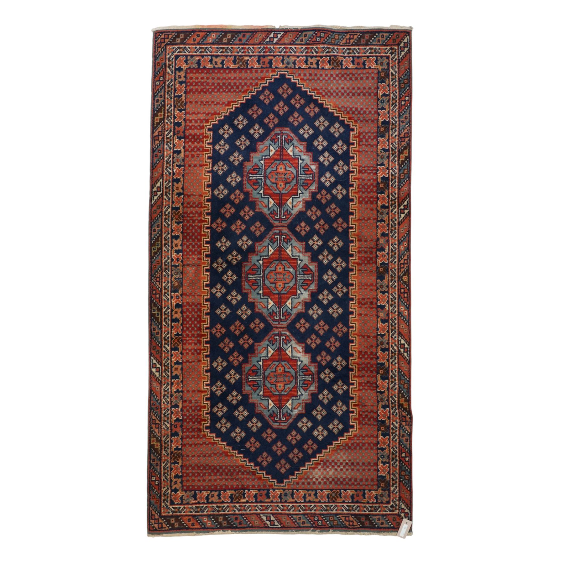 North West Persian Heriz hand-knotted rug, indigo field with three central stepped geometric medallions arranged vertically, enclosed by angular spandrels and multiple geometric borders in shades of madder red, ivory, and pale blue, with cotton fringe ends  