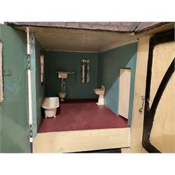 Large Tri-ang No.93 doll`s house in the 'Stockbroker's Range' c1935; two-storey double-fronted Tudor design, half timbered gables, two-storey bay windows, cream and mock shrubbery to front, opening metal framed windows with green shutters, red simulated tiled roof with chimney, integral garage with opening doors, front elevation has four hinged doors opening to reveal two bedrooms with fire places, living room, bathroom and kitchen with built in dresser and sink, entrance hall and staircase, side entrance with porch and seat and sun dial over on chimney stack; some wiring for electrical lighting; metal Tri-ang Toys disc verso; comprehensively furnished H66cm L117cm D43cm