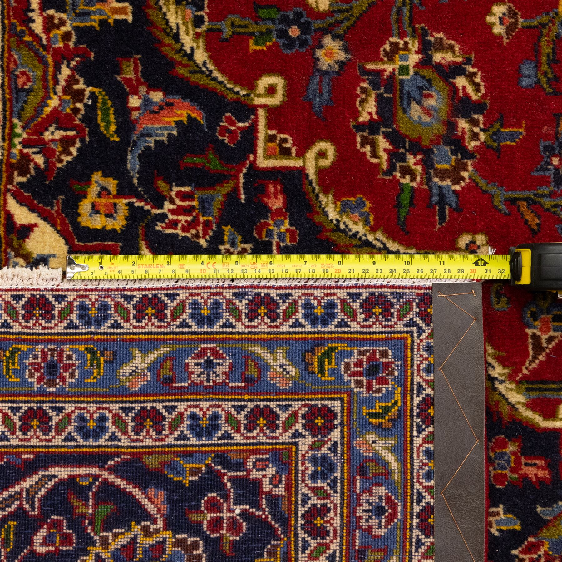 Central Persian Kashan hand-knotted carpet, crimson ground, with a central shaped palmette medallion with pendants, surrounded by scrolling foliate and floral motifs incorporating rosettes, palmettes, and vine work, enclosed by a dark navy with repeating border with repeating palmettes and meandering vines, flanked by floral guard stripes, with cotton fringes 