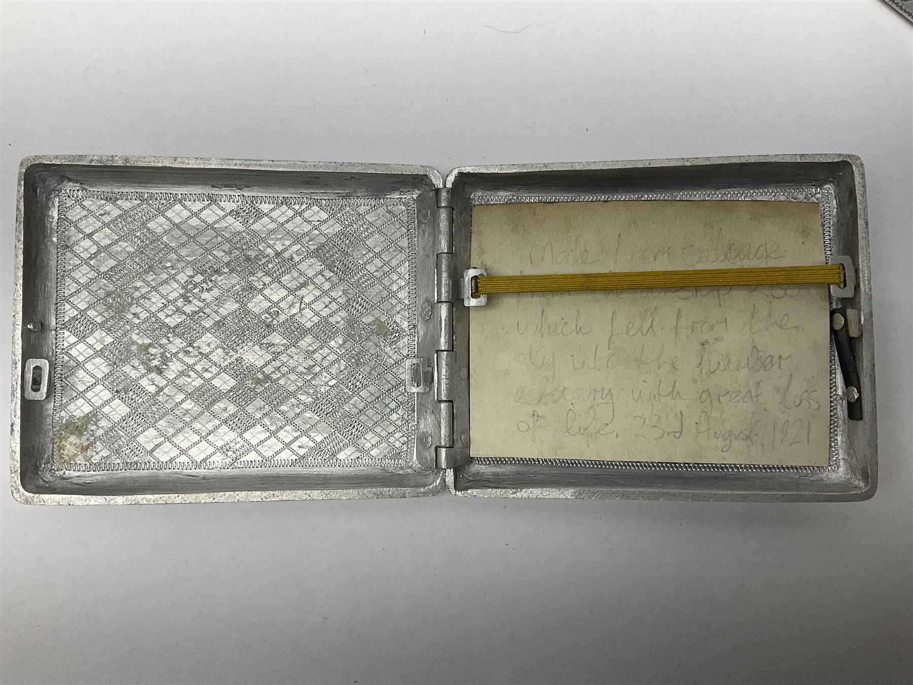 Aluminium cigarette case, by repute made from the R.38. Airship wrecked over Hull August 24th 1921, together with a aluminium matchbox cover, the front inscribed 'R38 WRECKED AT HULL 24 AUG 1921 44 LIVES LOST', the event illustrated verso, (2)