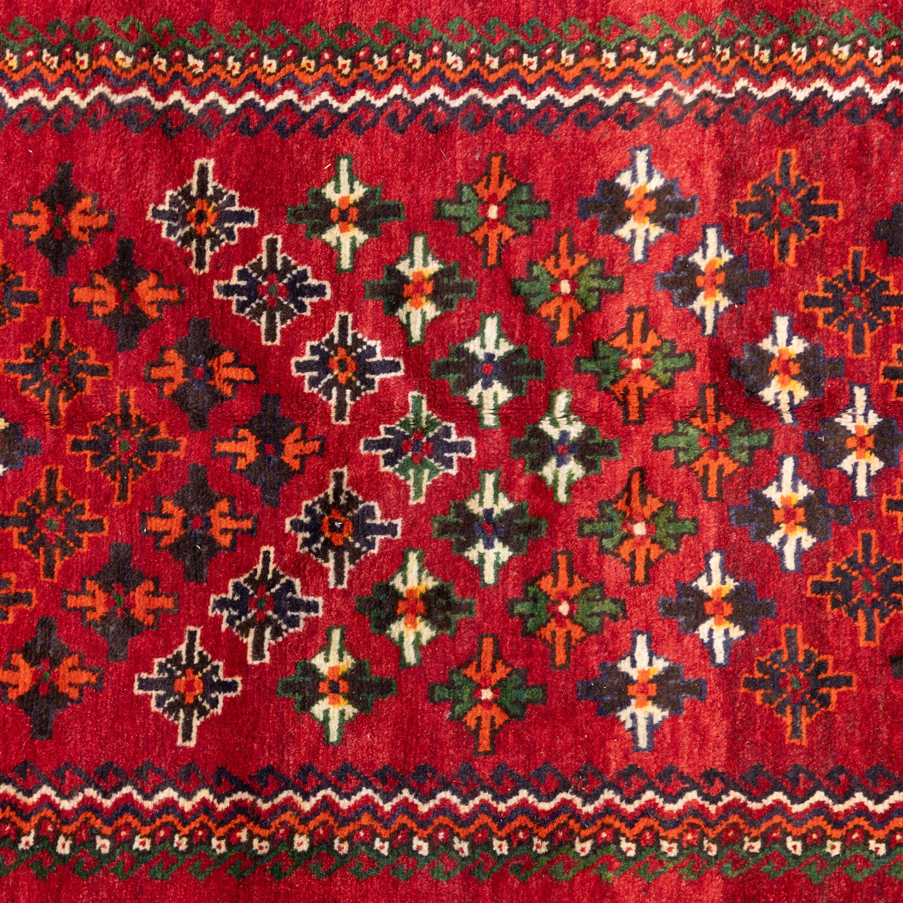 South West Persian Lori hand-knotted rug,  deep crimson field with a stepped lozenge medallion enclosing stylised floral motifs within multiple geometric borders of indigo, ivory, and green, with fringe ends 