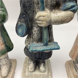 Three Chinese terracotta court attendant tomb figures, probably Ming Dynasty, two examples decorated in Sancai green glaze, the third example decorated in two tone blue glaze, each upon stepped square bases, tallest H22.7cm