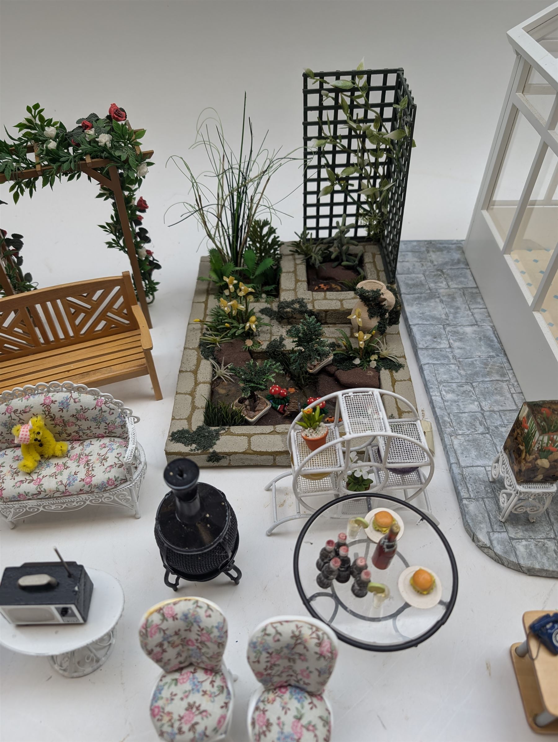 1:12 scale dolls house conservatory and garden accessories, including white wooden glazed conservatory on a stone effect base, black and white metal garden seating, barbecue, plant shelves, parasol, barbeque accessories, large planters, rabbit hutch, animals, chimenea, etc