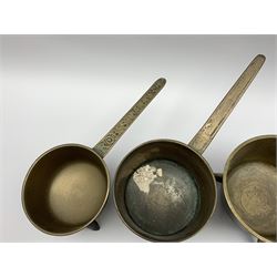 Four 18th and early 19th century bronze skillets upon outswept tripod legs, one example with handle cast 'Warner' 4P, another example with handle cast 'Rob Street & Co, and another with motto 'Praise God For All', largest L40cm