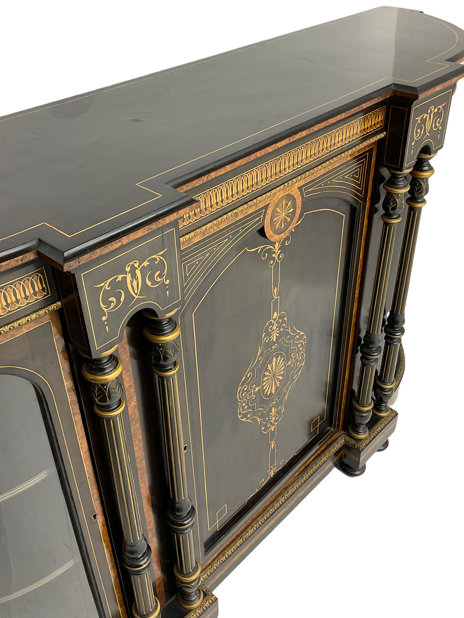 Victorian ebonised and inlaid credenza, break-front with curved ends, the front fitted with two curved glazed doors and central panelled door, inlaid with scrolling foliate and star motifs, quadruple turned and fluted pilasters to front, gilt egg and dart moulded edge on plinth base with figured walnut band, on turned feet