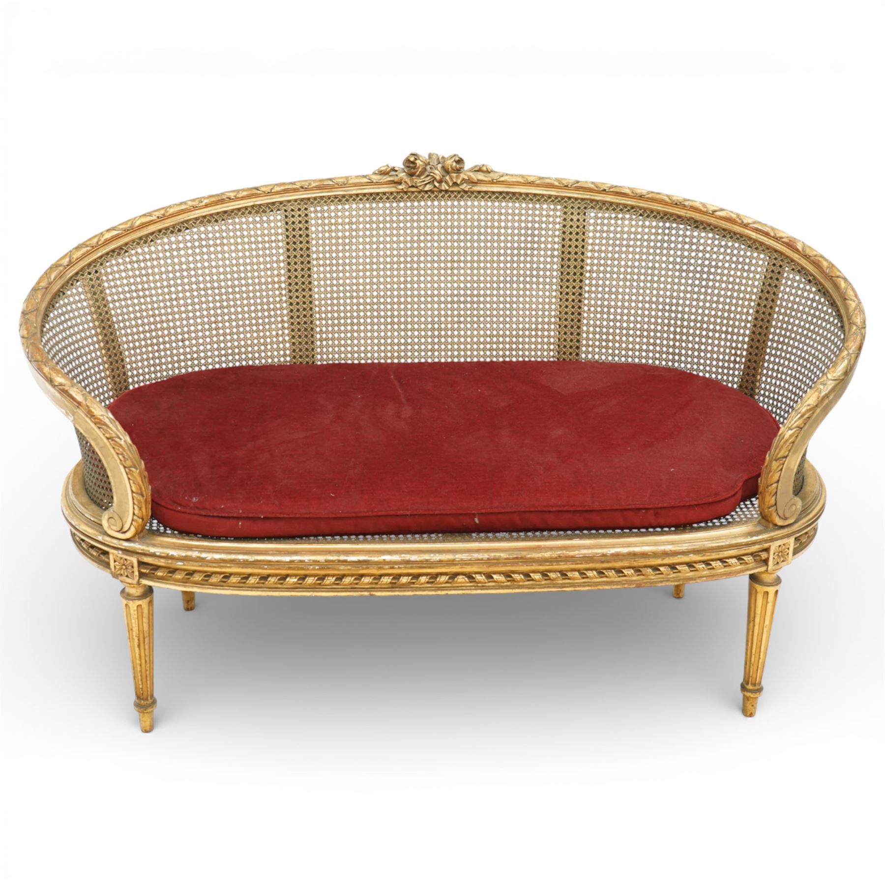 19th century giltwood and gesso settee, with shaped crest rail centred by carved floral detail, the cane back with vertical divisions, upholstered seat with loose cushion, raised on fluted tapering legs