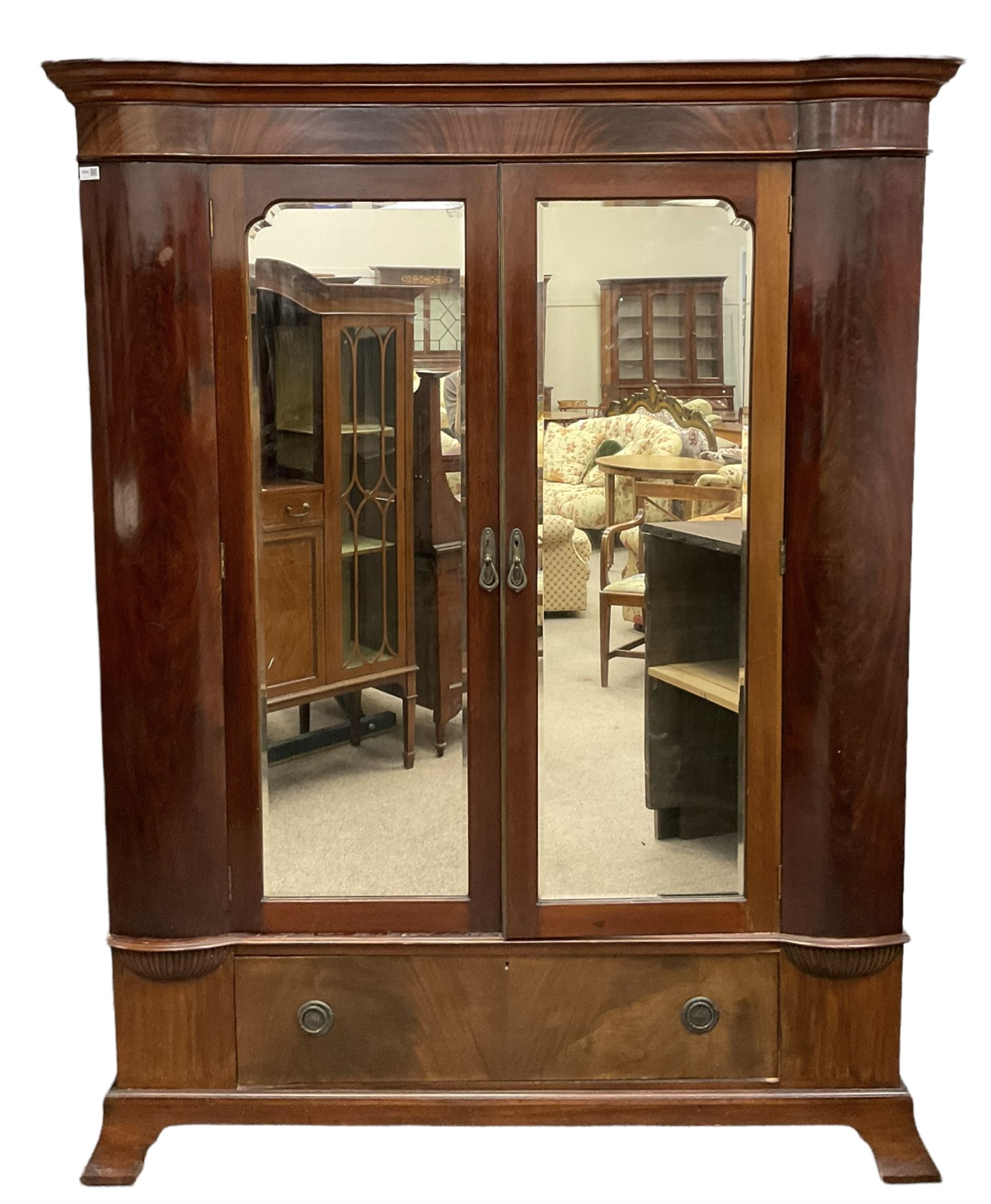 Late 19th century mahogany double wardrobe, projecting cornice over figured frieze, curved uprights enclosing two doors with bevelled mirrors, drawer to base, on splayed bracket feet