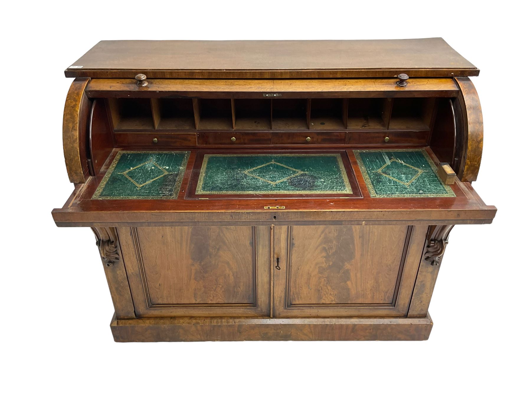 Victorian mahogany roll-top writing desk, top concealing fitted interior with pigeonholes and three drawers, the trisector inset writing surface with writing slope, base fitted with panelled cupboard enclosing single shelf, decorated with scrolled corbels