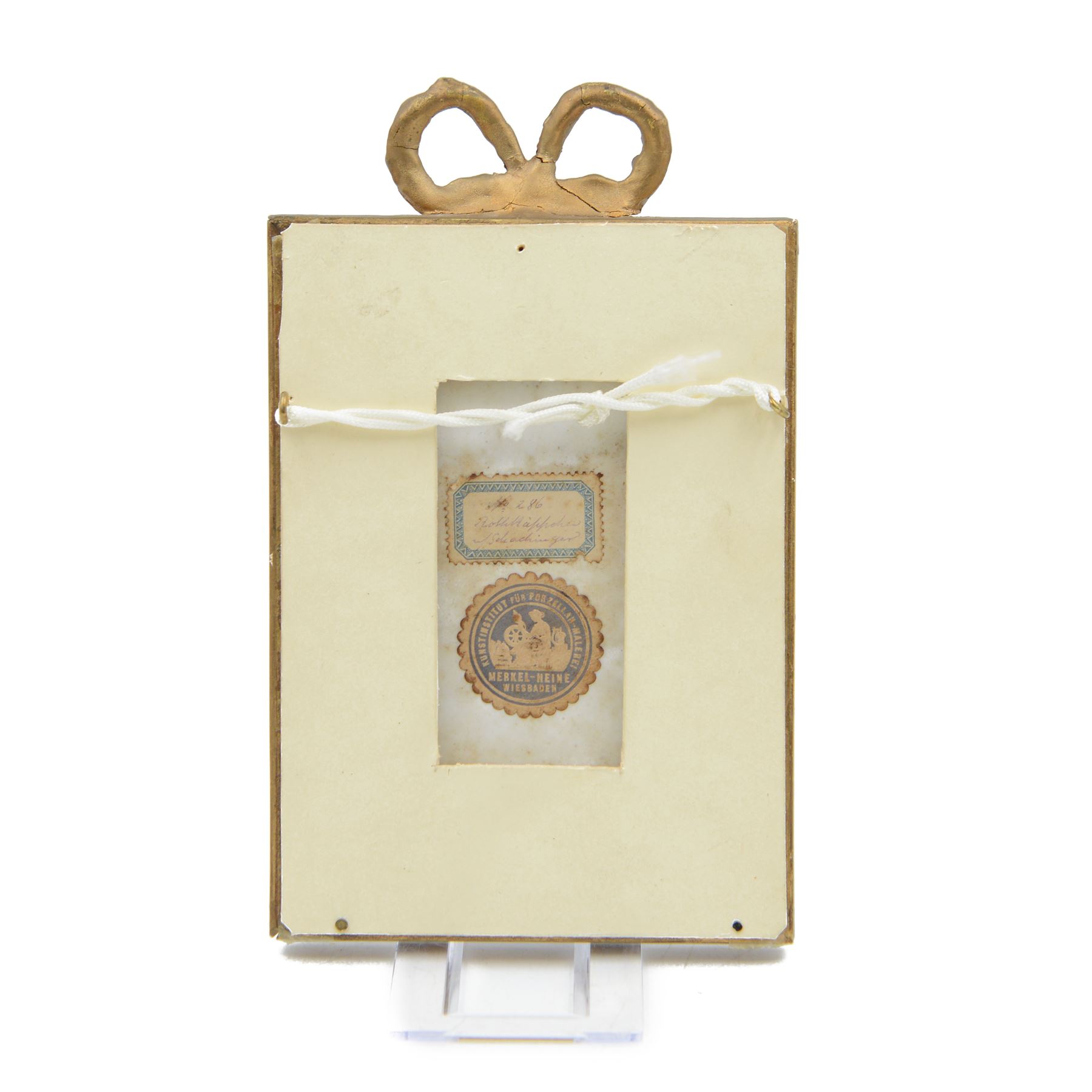 Late 19th/early 20th century German hand painted porcelain plaque, depicting a young girl in a red bonnet, after a painting by Gabriel Schachinger, within a beaded gilt frame with bow surmount, bearing paper label for Kunstinstitut fur Porzellan-Malerei Merkel-Heine Wiesbaden verso, and further paper label indistinctly inscribed '286 [...] Schachinger', also impressed 107, not including bow 16cm x 11.5cm
