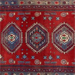 Caucasian Kazak rug, red field decorated with a column of stepped hexagonal medallions in blue, ivory, and crimson, flanked by stylized floral and geometric motifs, enclosed by multiple borders of rosettes and hooked designs 