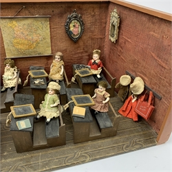 Late Victorian wooden school room setting with bisque head teacher and six German all bisque pupils each seated at a combined desk and chair with slate board, in a classroom furnished with chest of drawers, fire-surround, lectern, wall map, pictures, miniature books, school bell, chalk board on easel, wall clock etc, L70cm H28cm D28cm