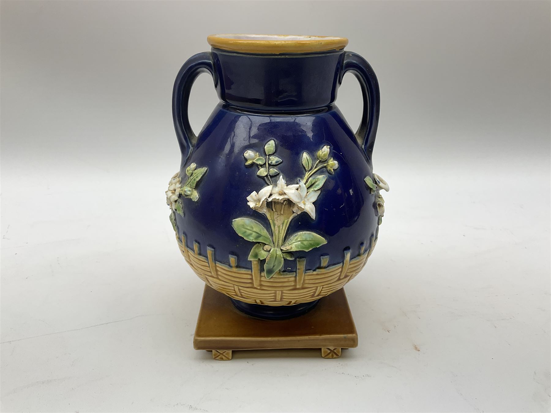 Minton majolica vase, the squat body with twin handles, with part osier moulding and applied Spring flowers against a cobalt blue ground, upon integral square base, impressed beneath Minton 1316, H16.5cm