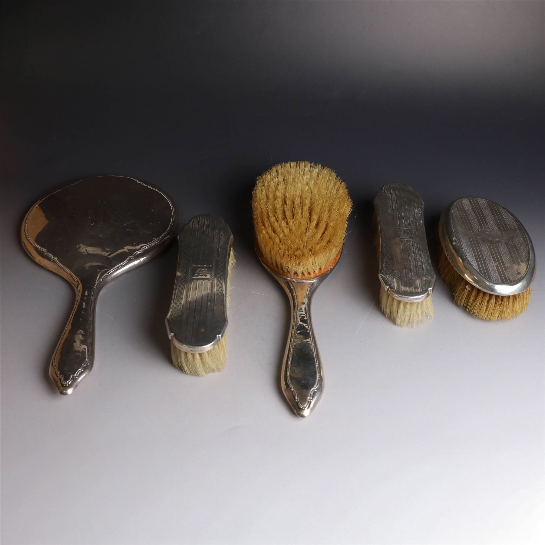 Five silver mounted dressing table items, including 1920s mirror and hairbrush set, with engraved initial to reverse, pair of clothes brushes with engraved initials and engine turned decoration and an oval clothes brush, all hallmarked 