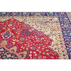 North West Persian Tabriz hand-knotted carpet, madder red field with a central cusped medallion issuing radiating pendants and an all-over design of scrolling arabesques, palmettes and flowering vinery enclosed by conforming spandrels, indigo main border of meandering floral vines and stylized palmettes, flanked by narrow guard stripes, cotton fringe ends 