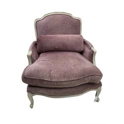 Louis XVI style bergere enclosed armchair, white finish shaped and moulded frame carved with scroll and foliate detail, upholstered in purple fabric with loose seat cushion and additional bolster cushion, serpentine seat, on cabriole supports