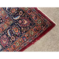 Persian Meshed carpet, plum ground and decorated with stylised flower heads and interlacing foliate, large central stylised medallion with orange detail, the orange mirrored in the five band border decorated with scrolling floral design, signature panel to end 