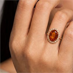 18ct gold citrine and diamond cluster ring, single oval cut citrine of approx 6.90 carat, surrounded by twenty round brilliant cut diamonds, stamped, total diamond weight approx 0.60 carat