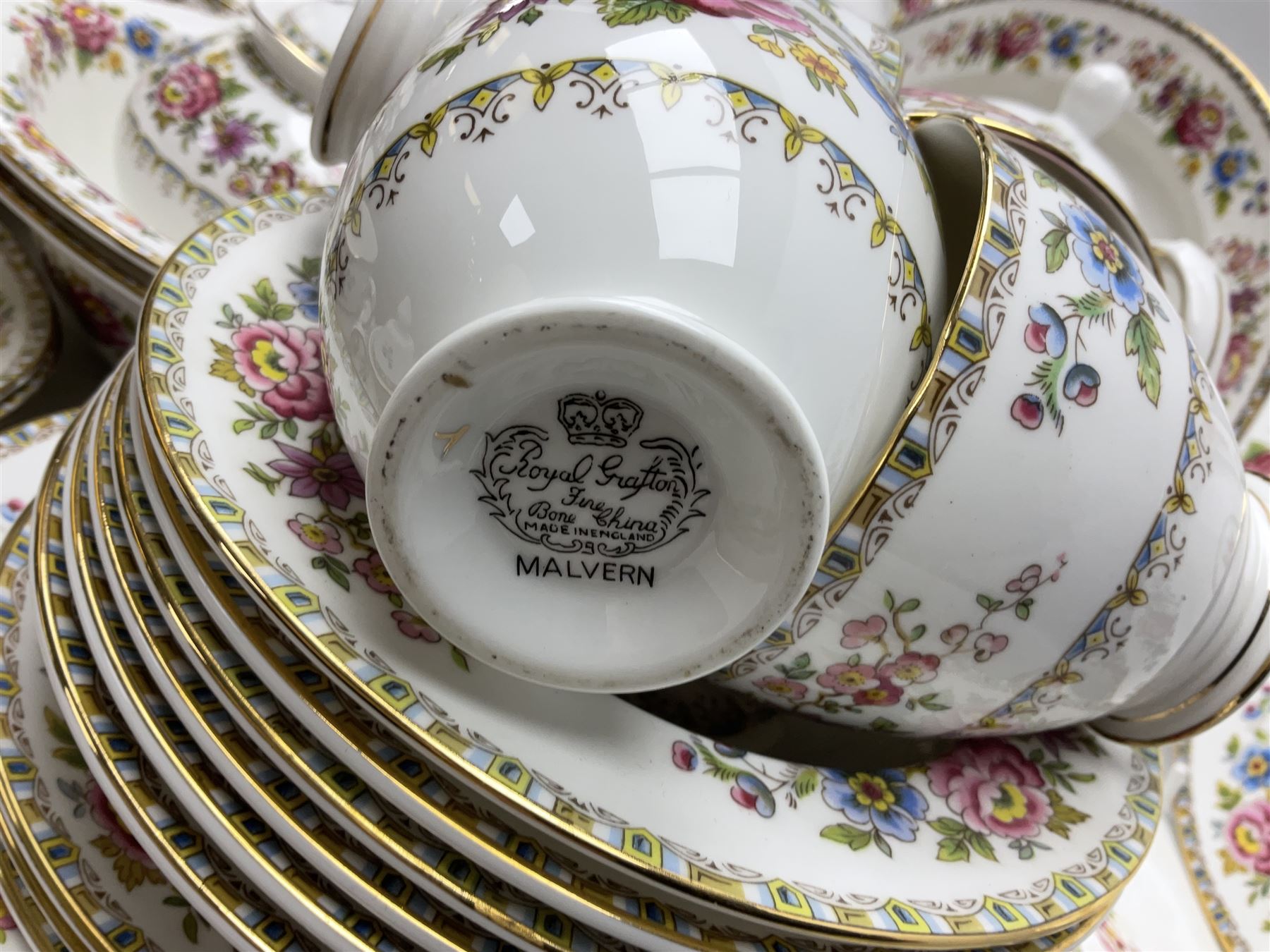 Extensive Royal Grafton Malvern pattern tea and dinner wares, comprising twelve dinner plates, six smaller plates, coffee pot, two teapots, two cake plates, eight teacups and ten saucers, six coffee cups and six saucers, two open sucriers, twin handled lidded sucrier, jug, lidded mustard pot and condiment jar, lidded tureen, two circular twin handled vegetable tureens, sauce boat and stand, oval and circular serving plates, salt and pepper shakers, breakfast cup and two saucers, further large cup and saucer, eighteen tea plates of various shapes, six side plates, six cereal bowls and six further bowls, shell dish and dish of square form, fork and knife, together with a hallmarked silver condiment spoon