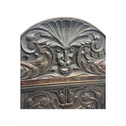 Late 19th century Jacobean revival carved oak armchair, the tall back with arched cresting featuring a stylised foliate mask, flanked by carved scrolls, relief carved panel depicting symmetrical foliage, downscrolled arms, on turned front supports united by stretchers