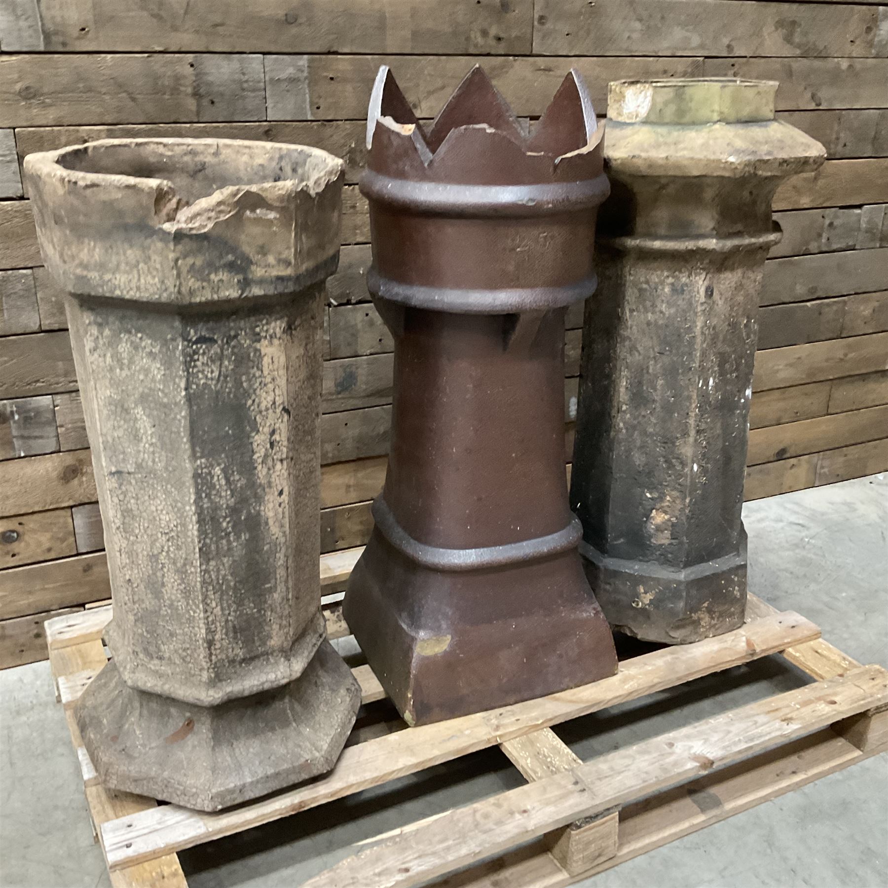 Collection of three Victorian and early 20th century reclaimed terracotta chimney pots, comprising: one cylindrical form with weathered, cracked glaze and flared octagonal base; one deep red cylindrical pot with fluted midsection and castellated rim, bearing moulded number ‘25’; and one tapering hexagonal example with wide flared rim and weathered patina. All with age-related wear and chips, consistent with use and outdoor exposure. Plus a selection of cast stone pieces including fountain 