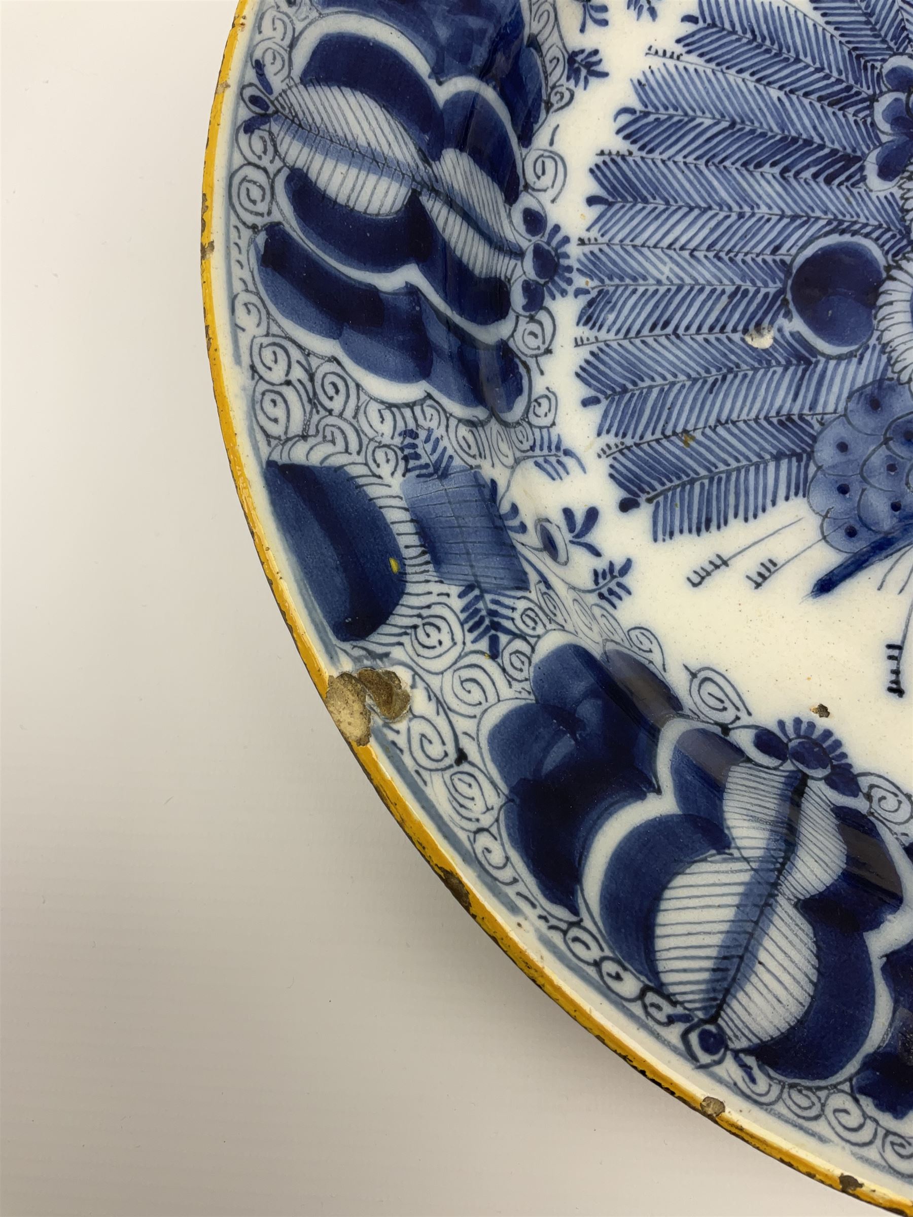 18th century Delft blue and white peacock pattern dish, painted with a fan of peacock feathers behind an urn of fruit and flowers, D34.5cm. 