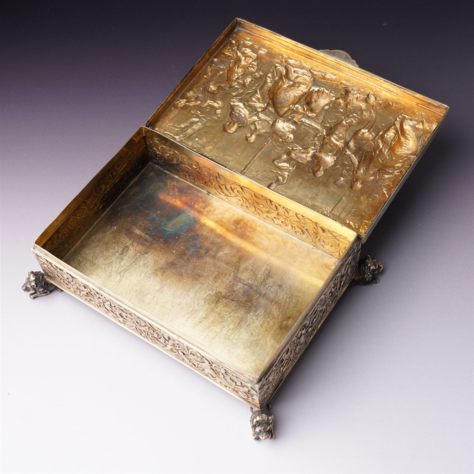 German 800 standard silver gilt and ivory mounted box, the hinged cover embossed and chased with an allegorical feasting scene, the sides with floral decoration, on four cast lion feet 21cm x 16cm x 8cm Maker Ludwig Neresheimer, Hanau circa 1900 This item has been registered for sale under Section 10 of the APHA Ivory Act