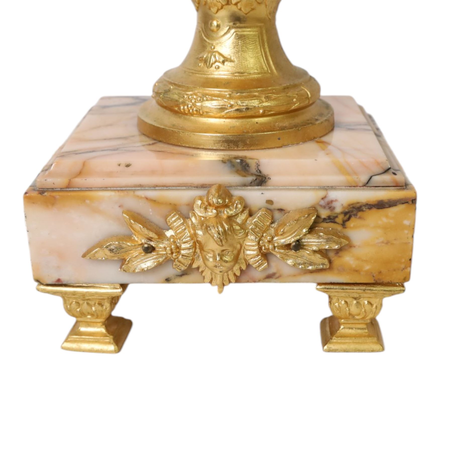 Pair of Rococo style gilt metal table lamps, the urn shaped bodies each with applied figure seated upon shoulder, and female mask to opposite side issuing scroll leading to top of neck, the body cast and applied with stiff leaf detail, and foliate swags and wreaths, upon square pink marble plinths with applied gilt metal mask mounts, and four gilt metal bracket feet, each supported a pleated cream silk closed top lampshade, H63cm