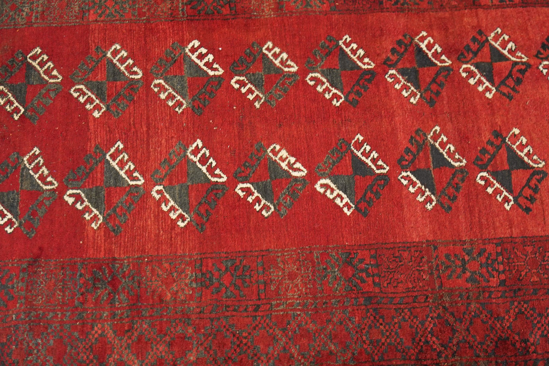 Afghan Turkoman crimson ground rug decorated with twin rows of hooked geometric guls within broad compartmented geometric borders (125cm x 201cm); Afghan Bokhara rug with repeated octagonal guls on a terracotta ground, enclosed by multiple geometric borders and patterned elem panels (120cm x 192cm) (2)