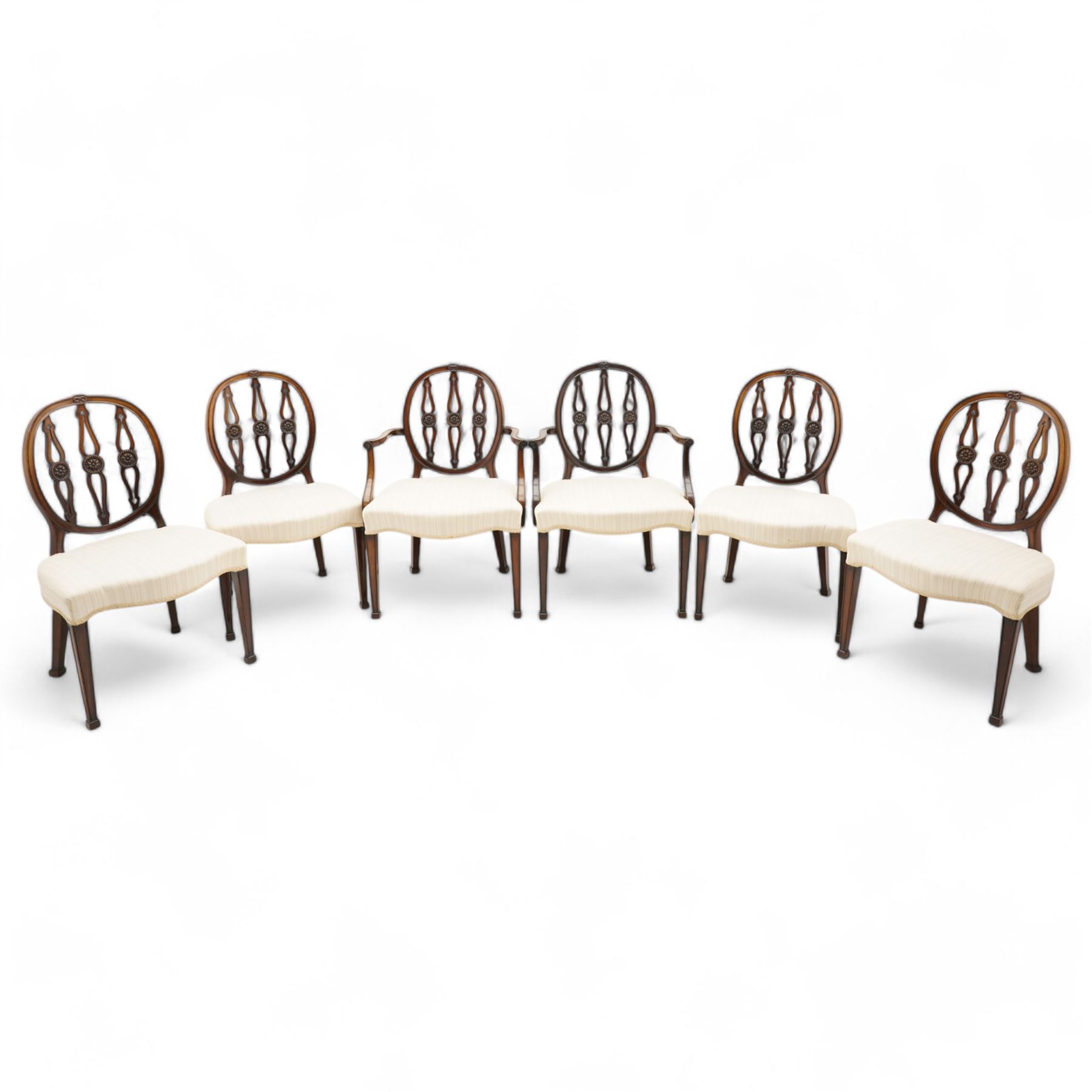 Set of six (4+2) late 19th to early 20th century Hepplewhite design mahogany dining chairs, moulded oval framed back with three shaped and pierced upright rails decorated with floral carved roundels, upholstered in pale fabric, on square tapering supports with recessed panels and block feet 